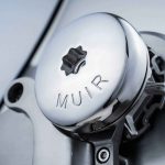 Precision-machined metal component with "MUIR" engraved, highlighting engineering craftsmanship.