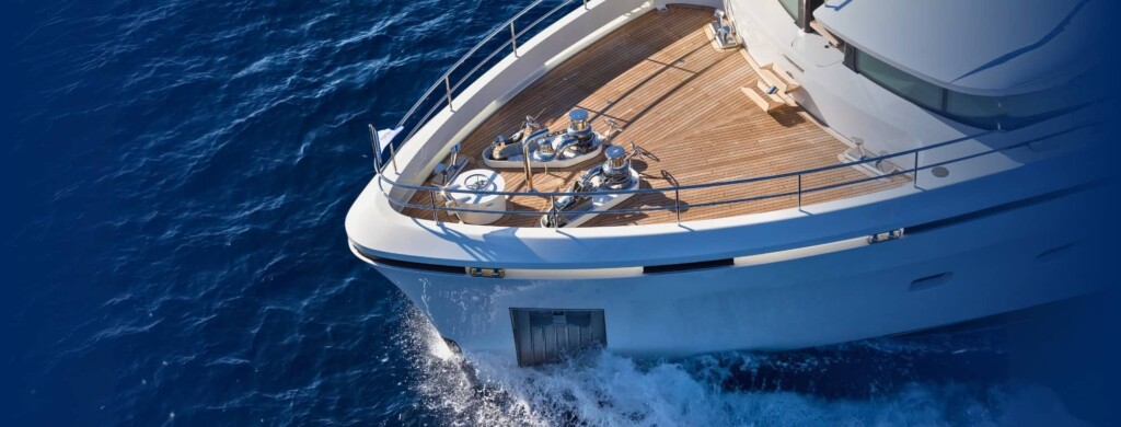Marine engineering yacht deck with stainless steel winches and wooden flooring in blue ocean waters.